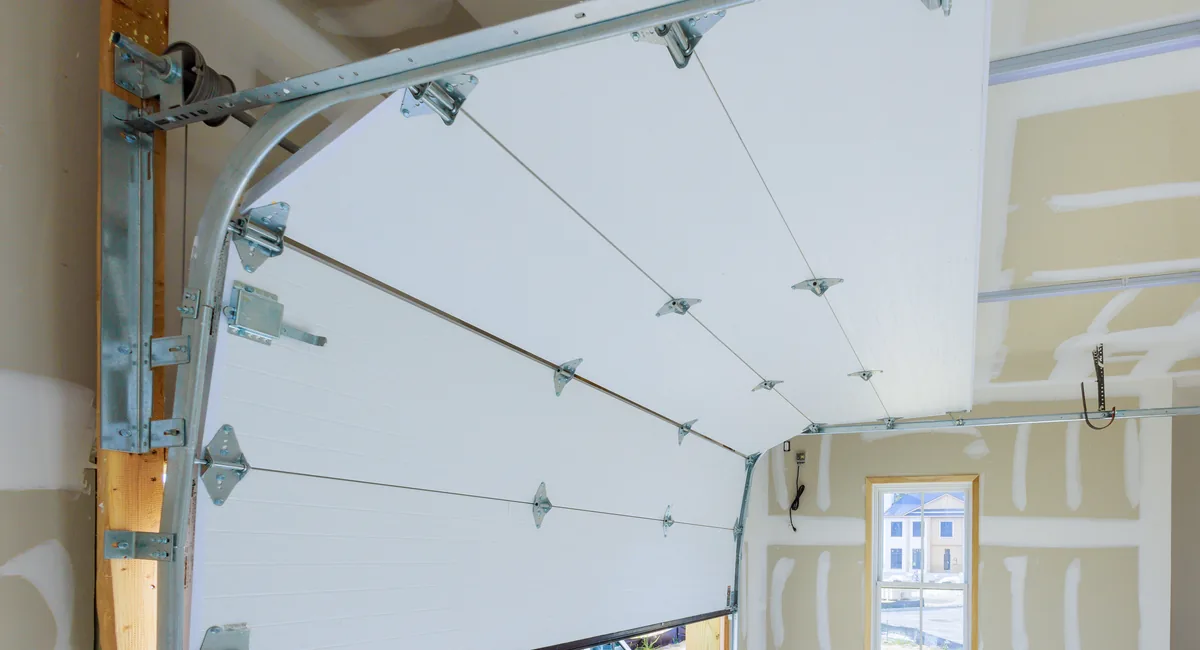 Newly installed white sectional garage door with track and spring hardware inside a garage